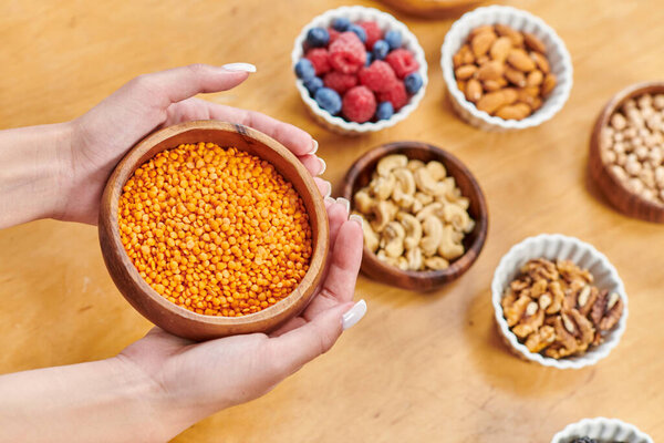 обрезанная женщина с миской чечевицы рядом с различными ягодами и орехами на столе в домашних условиях, растительная диета