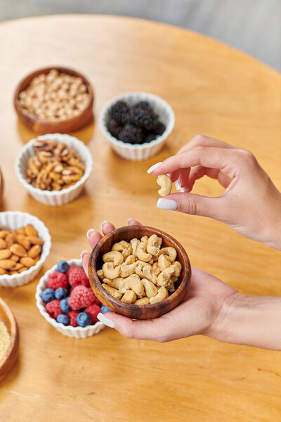 обрезанный вид вегетарианки с миской кешью над здоровой растительной пищей на столе