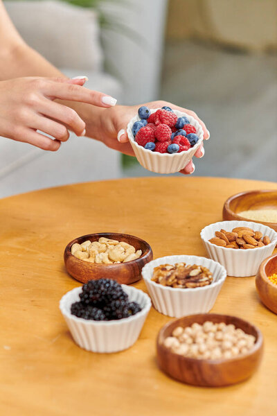 обрезанная женщина указывает на чашу со свежей клубникой и черникой возле различных вегетарианских блюд