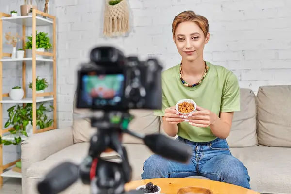 vegetarian woman with bowl of almonds near fresh blackberries and blurred digital camera, video blog