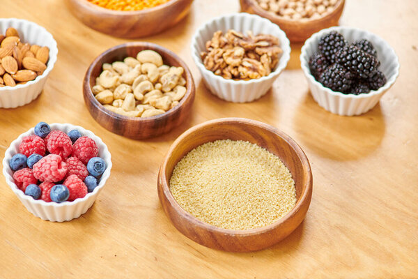 чаша с кускусом рядом с различными орехами и свежими ягодами на столе, концепция питания растительного происхождения