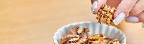 cropped view of woman taking walnut from white ceramic bowl, vegetarian concept, horizontal banner