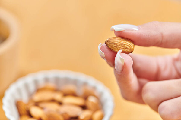 закрыть вид женской руки с миндалем над миской с вегетарианской пищей на размытом фоне