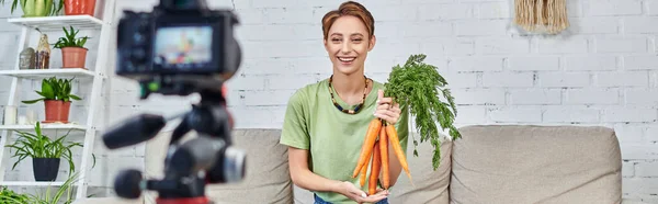 happy vegetarian woman with fresh carrots near blurred digital camera, vegetarian video blog, banner