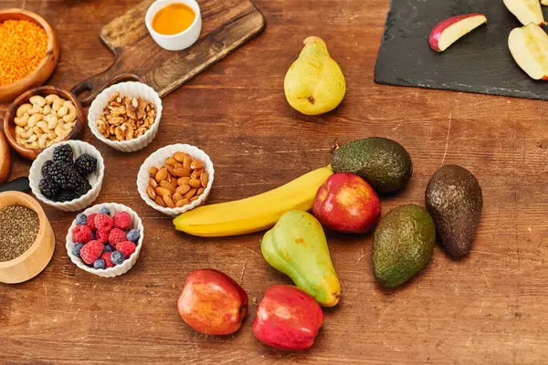 stock image top view of fresh fruits and assortment of nuts near cutting boards on wooden table, vegetarian diet