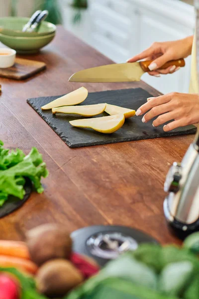 stock image partial view of vegetarian woman with knife near ripe sliced pear on chopping board in kitchen