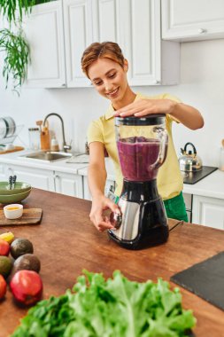 Elektrikli blender 'da taze meyve öğüten neşeli vejetaryen kadın, lezzetli meyve püresi tarifi.