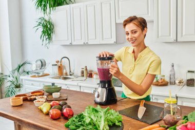 Vejetaryen kadın taze meyve ve sebzelerin yanında elektrikli blender ile smoothie hazırlıyor.