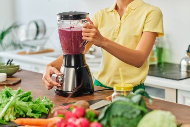 Vejetaryen meyve püresi hazırlayan ve blender 'da bitki kökü bileşenleri öğüten bir kadın görüntüsü.
