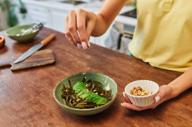 cropped woman adding walnuts into vegetarian salad with seaweed and sliced avocado, plant-based diet clipart