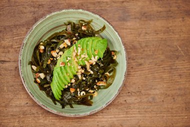 delicious vegetarian salad with seaweeds and sliced avocado with walnuts on wooden table, top view clipart