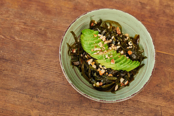 вид вегетарианского салата с водорослями и нарезанным авокадо с грецкими орехами на деревянном столе