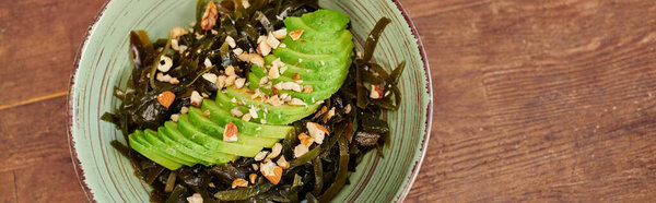 bowl with vegetarian salad with seaweeds and sliced avocado with walnuts on wooden table, banner