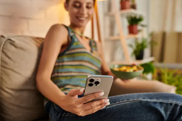 stock image blurred vegetarian woman taking selfie while sitting with salad bowl on couch in living room