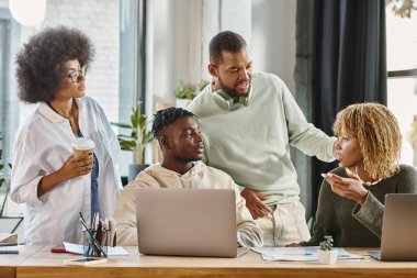 İyi görünümlü arkadaşlar planlarını masadaki grafikler ve dizüstü bilgisayarlarla aktif olarak tartışıyorlar.
