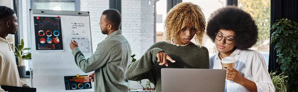 two women looking at laptop while their friends working on graphs on backdrop, business, banner