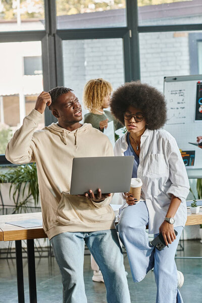 two puzzled coworkers working with laptop with their friend on backdrop, coworking concept
