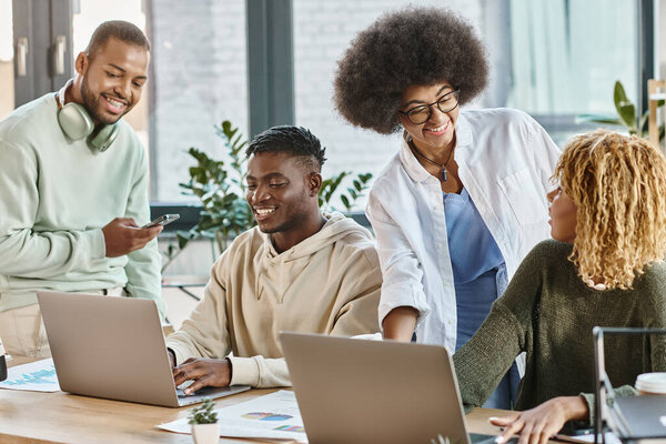 cheerful women smiling at each other with their male friends joyfully looking at laptop, business