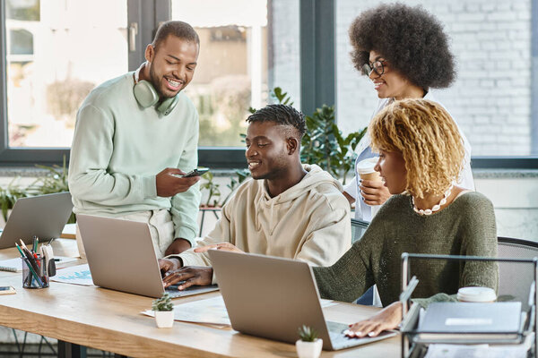 cheerful friends in casual bold outfits with coffee and phone in hands smiling happily, coworking