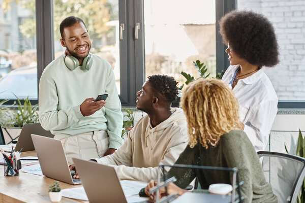 three good looking people looking attentively at their smiling friend with headphones, coworking