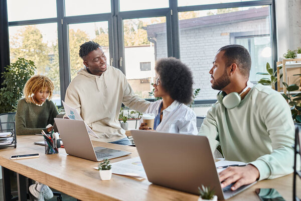 young stylish colleagues discussing their paperwork and graphs sitting at table, working concept
