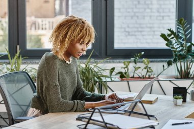 Dişlerinde diş teli olan neşeli Afro-Amerikalı kadın dizüstü bilgisayarda çalışıyor ve samimi bir şekilde gülümsüyor, iş konsepti.
