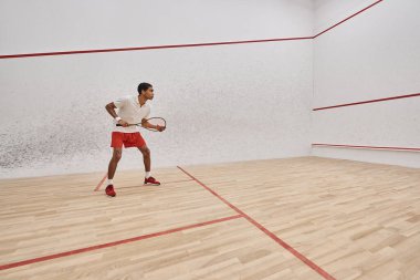 Yan bakış, atletik Afrikalı Amerikalı adam mahkemede oynarken squash raketi tutuyor.