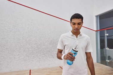 Atletik Afro-Amerikan sporcusu squash oynadıktan sonra elinde bir şişe su tutuyor.