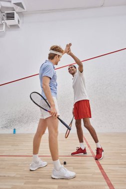 Spor giyim sektöründeki neşeli çok kültürlü arkadaşlar mahkemede squash oynadıktan sonra beşlik çakıyor.