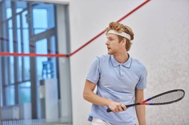 Spor salonunda squash oynarken raket tutan kızıl saçlı sporcu antrenman atışı yapıyor.