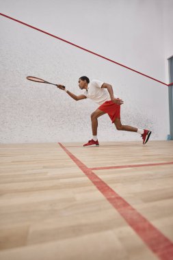 Elinde raket olan ve saray içinde squash oynayan enerjik Afro-Amerikan sporcusu.