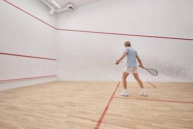 Mahkeme salonunda squash oynarken raket tutan kızıl saçlı ve sportif bir adam.