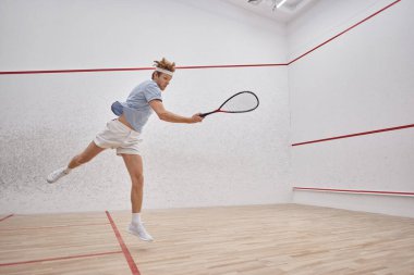 motion shot, energetic player holding racquet and jumping while playing squash inside of court clipart