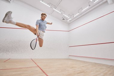 hareketli atış, raket tutan enerjik oyuncu atlarken ve mahkemede squash oynarken.