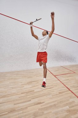 Hareketli atış, odaklanmış Afro-Amerikan sporcusu raketle atlayıp mahkemede squash oynuyor.