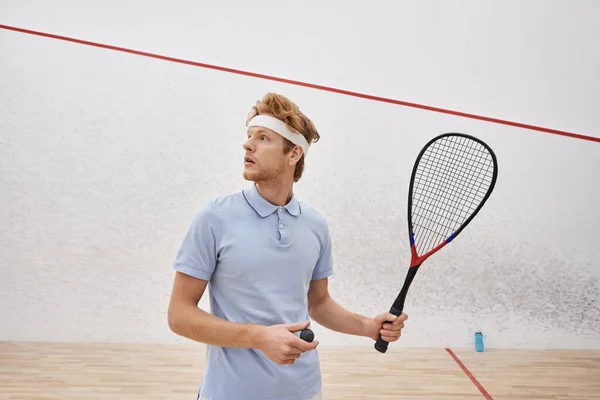 stock image redhead man in sportswear holding squash ball and racquet while standing inside of indoor court