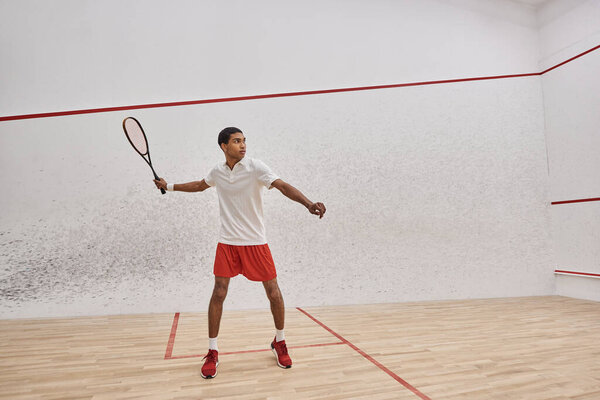 athletic african american man holding squash racquet and jumping while playing game in court