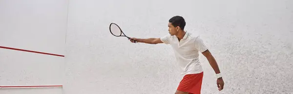 side view banner, athletic african american man in active wear holding racquet while playing squash