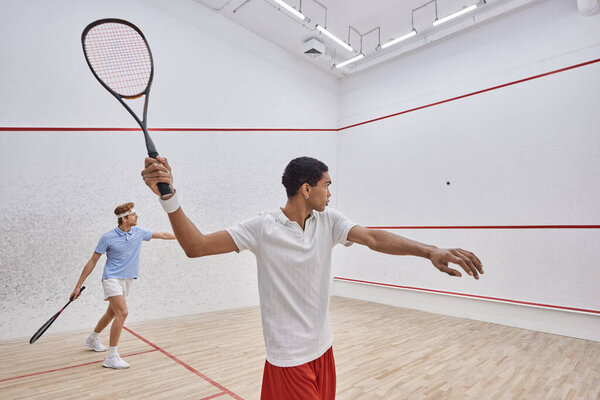 interracial players in sportswear playing squash together inside of court, active lifestyle