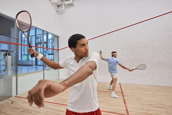 young interracial players in active wear playing squash together inside of court, lifestyle