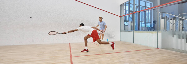 dynamic multicultural sportsmen playing squash together inside of court, sport and motivation banner