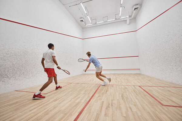 dynamic interracial sportsmen playing squash together inside of court, challenge and motivation