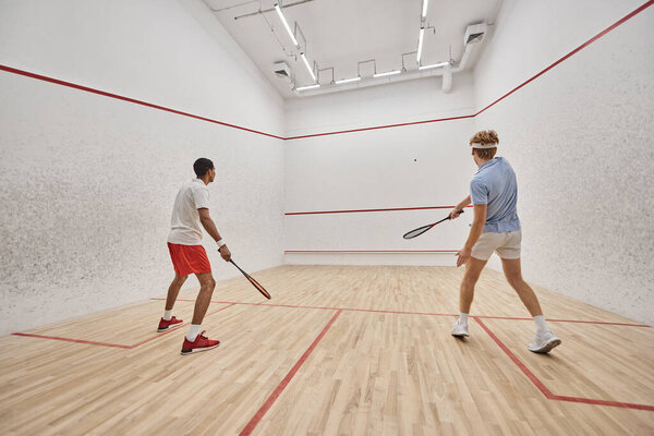 dynamic and interracial friends playing squash together inside of court, preparing for competition
