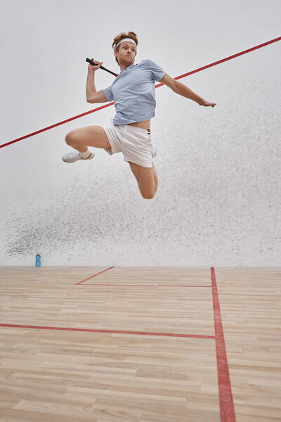 motion shot, active sportsman holding racquet and jumping while playing squash inside of court