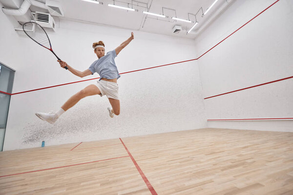 motion shot, active player holding racquet and jumping while playing squash inside of court