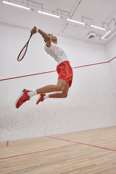 motion photo, active african american sportsman holding racquet while jumping and playing squash