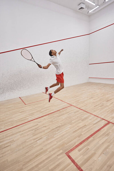 motion shot, active african american sportsman with racquet jumping and playing squash in court