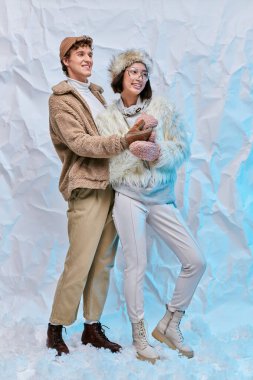Tasasız ırklar arası şık kış kıyafetleri içinde beyaz desenli arka planda kar seyreden bir çift.