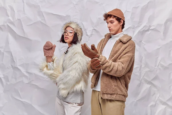 stock image man wearing warm gloves near asian woman in faux fur attire on white textured backdrop, winter style