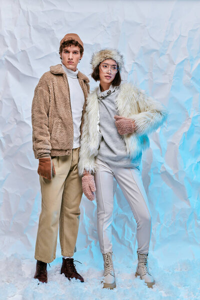 full length of interracial fashion models in cold-weather wear posing on white crumpled backdrop